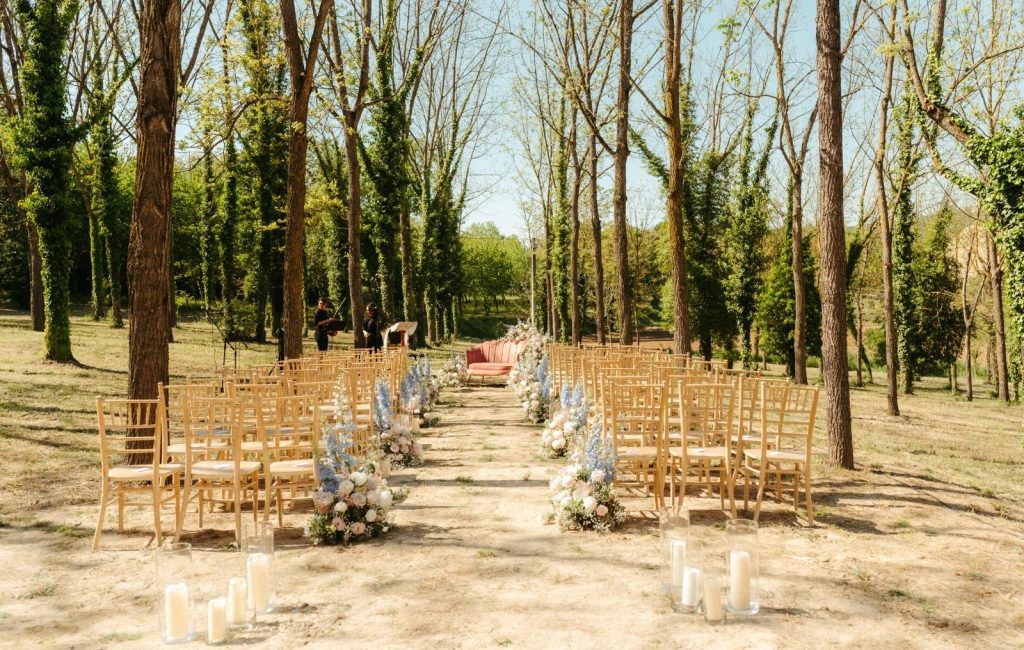 Cerimonia primaverile con sedie chiavari dorate, candele e alberi in fiore