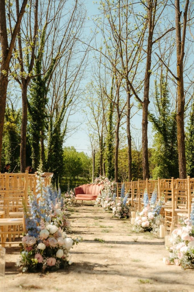 Cerimonia primaverile con sedie chiavari dorate, fiori blu e divano rosa