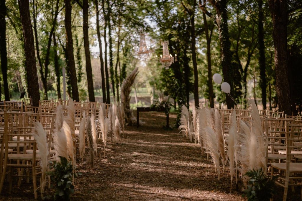 Cerimonia outdoor con sedie chiavari, decorazioni di pampas e lampadario tra gli alberi