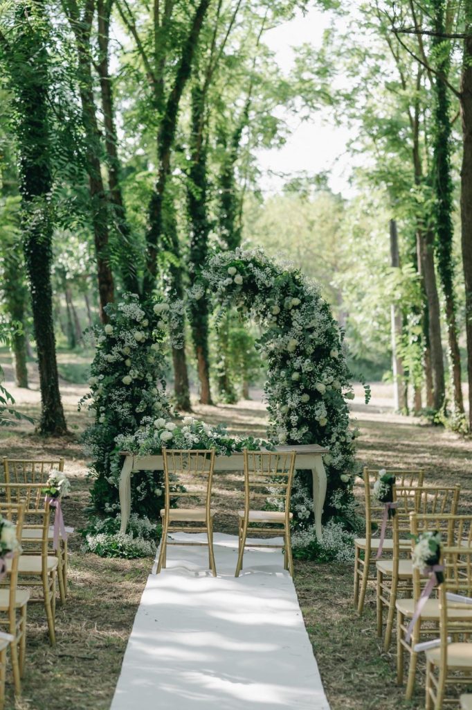 Cerimonia all'aperto con sedie chiavari dorate e arco verde monumentale