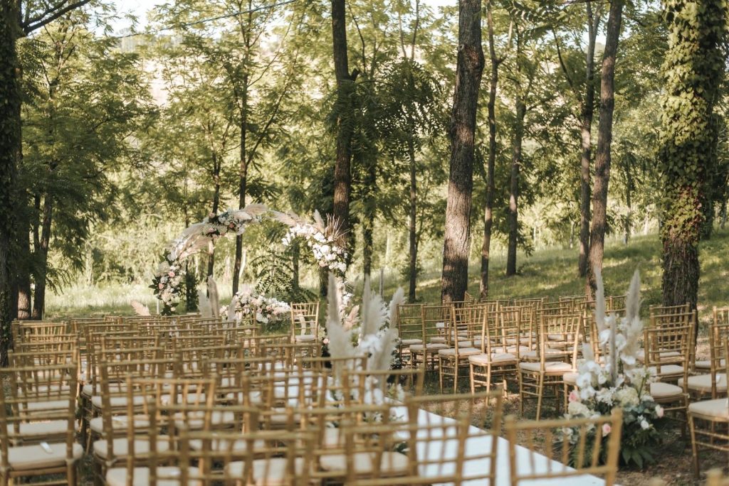 Cerimonia all'aperto con sedie chiavari dorate e arco bianco floreale al sole