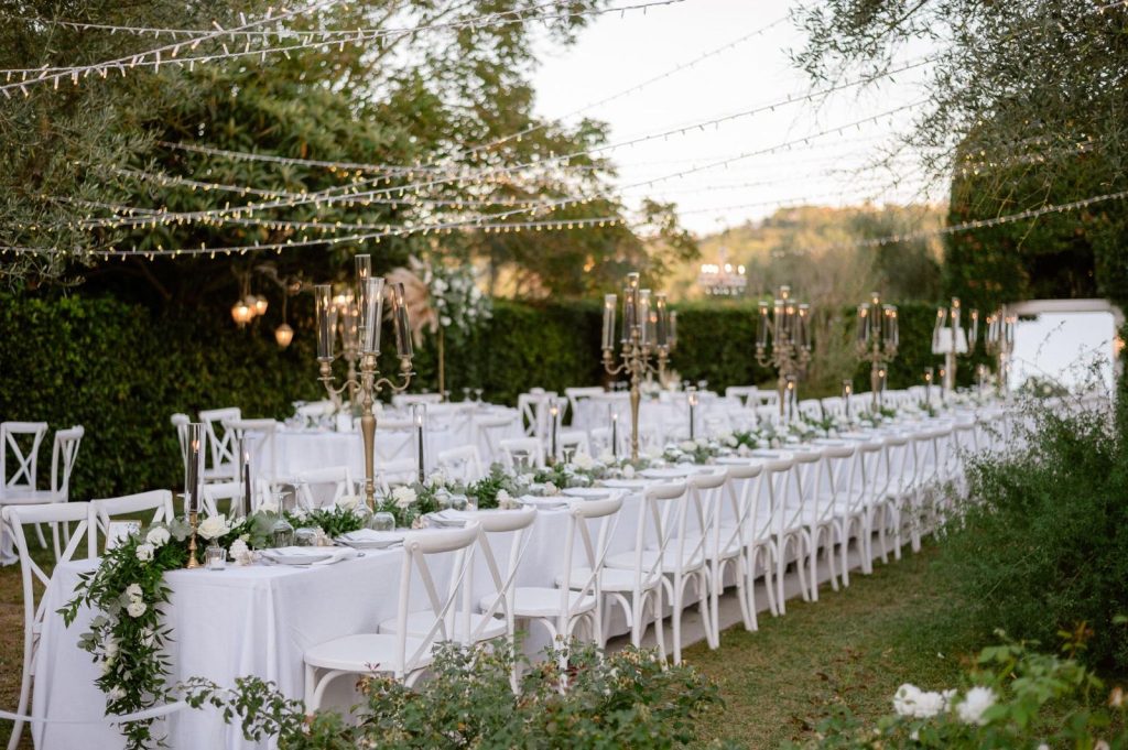 Banchetto serale tra gli ulivi con sedie crossback bianche e fairy lights