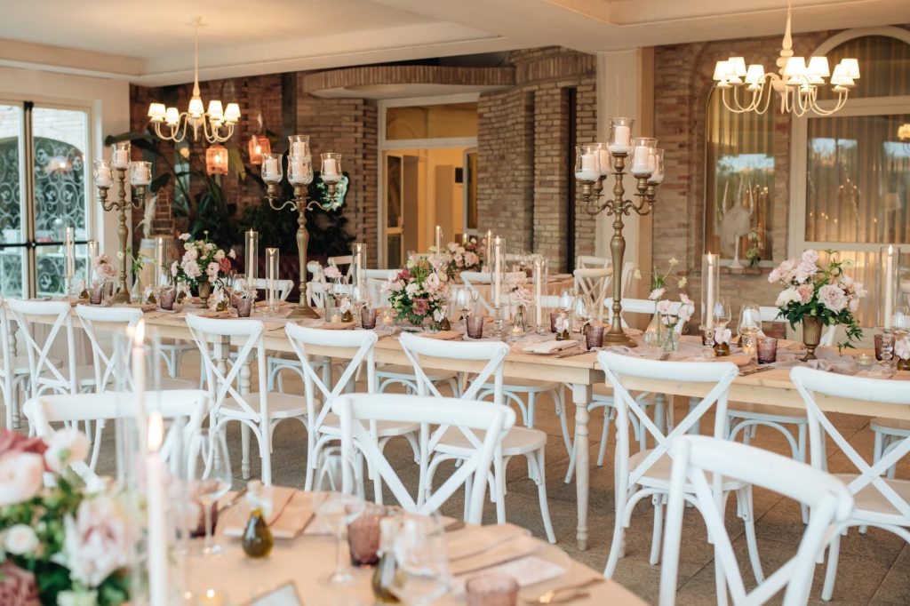 Sala interna con sedie crossback bianche, tavoli imperiali e candelabri dorati